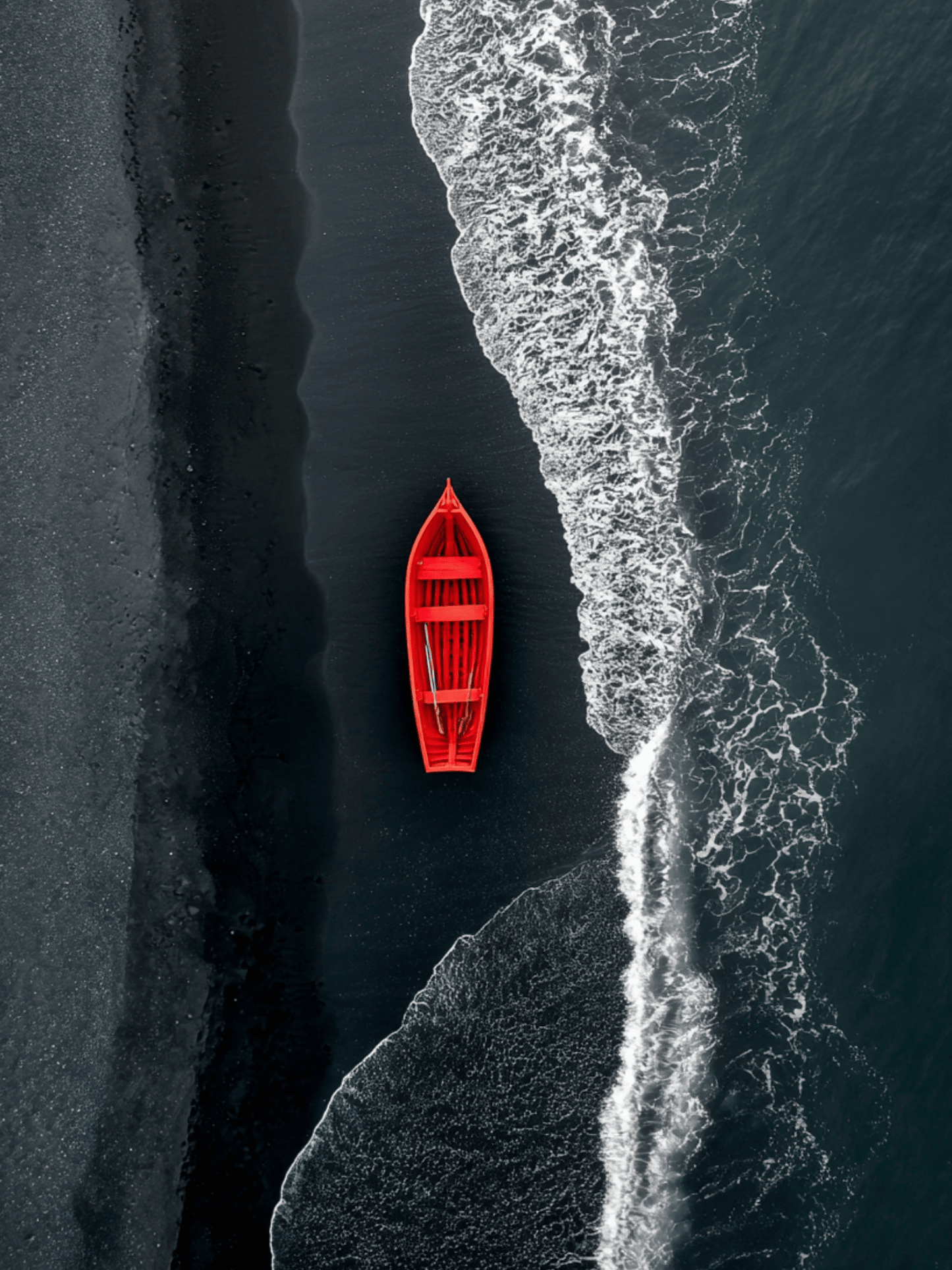Red boat on black sand shore