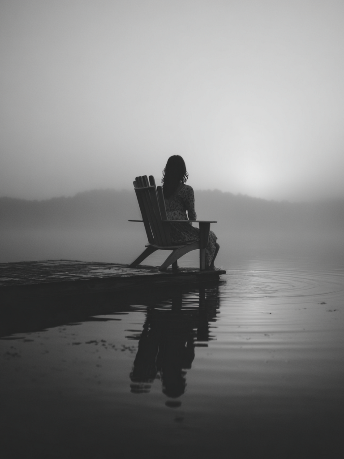 Woman sitting alone on dock in foggy lake sunrise